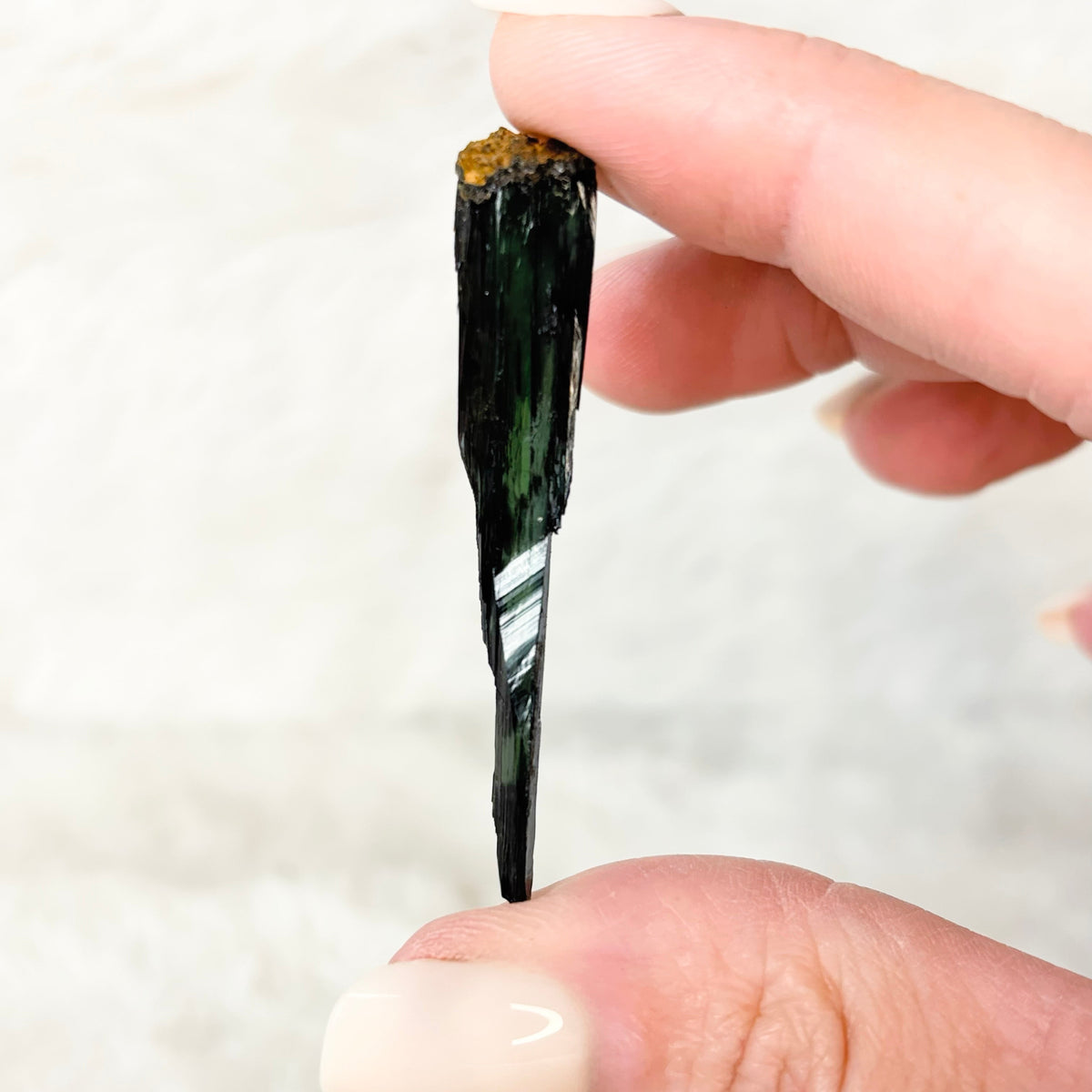 Hand holding a Vivianite specimen on a white background
