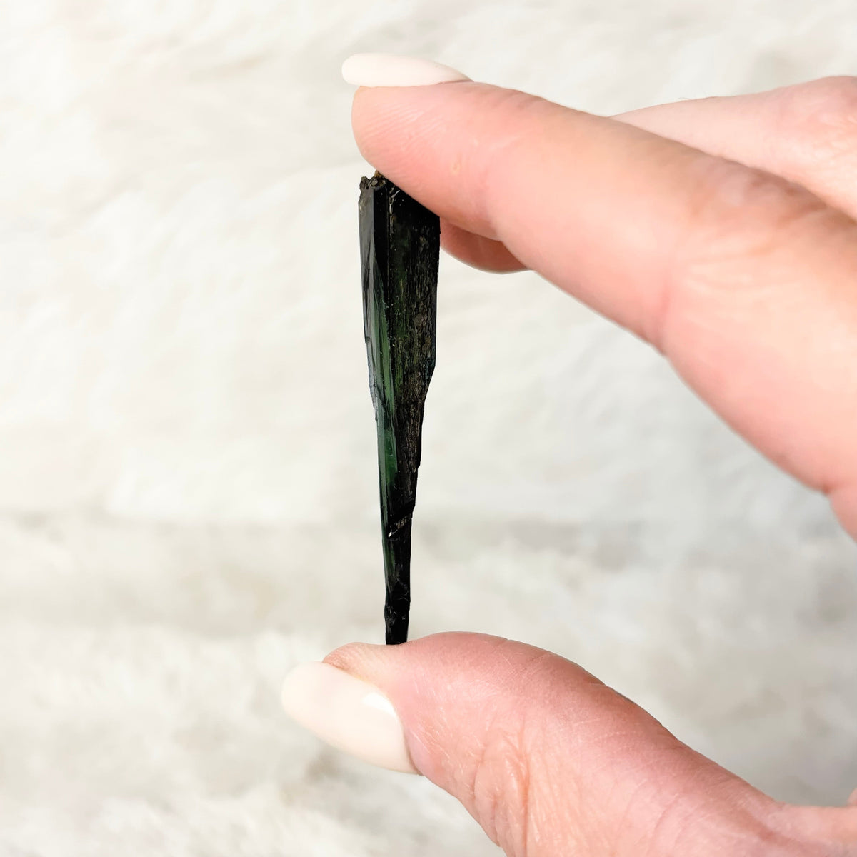 Hand holding a Vivianite specimen on a white background