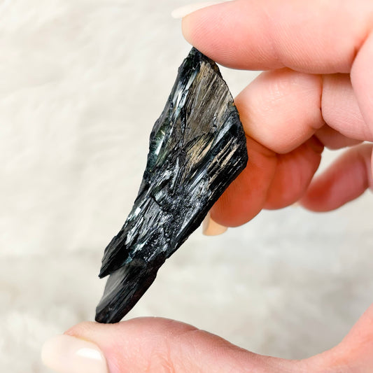 Hand holding a Vivianite specimen on a white background