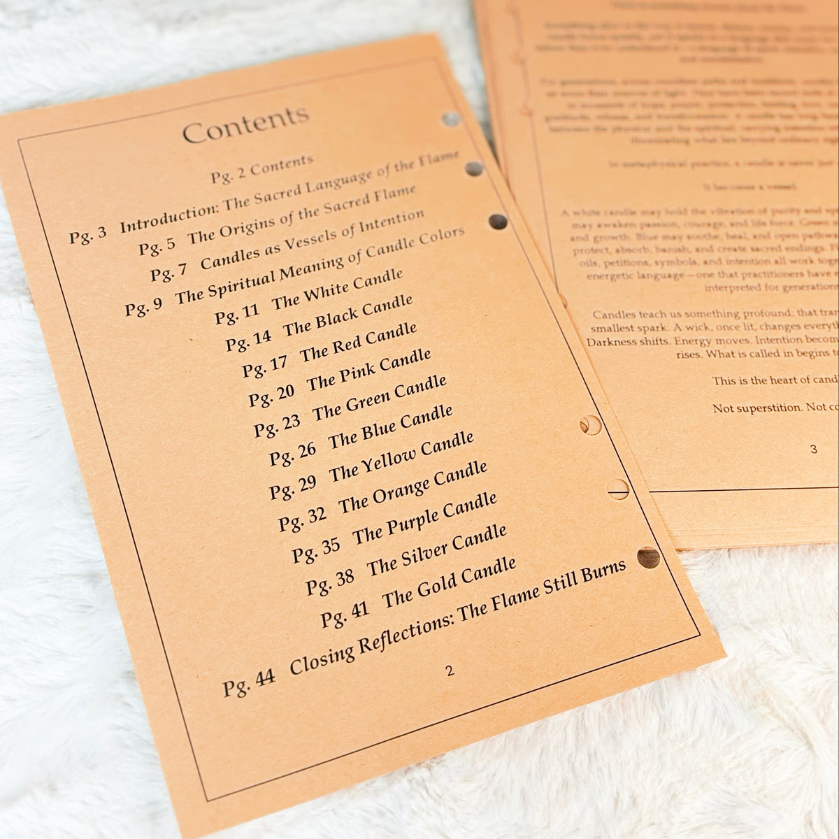 A printed booklet or instruction sheet titled 'Contents' with a list of candle chapters, placed on a white textured fabric next to another folded page.